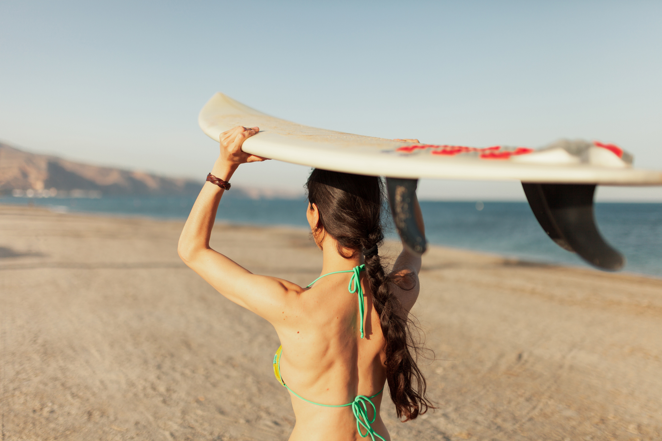 Woman with braid on the beach holding a surf board